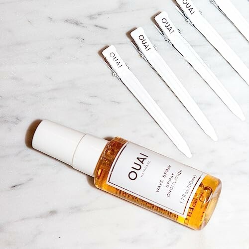 OUAI wave spray bottle on marble surface with hair clips.
